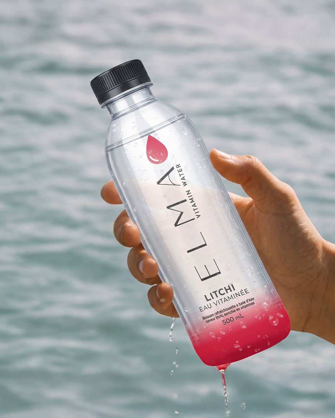 ELMA Vitamin Water lychee bottle held facing the sea